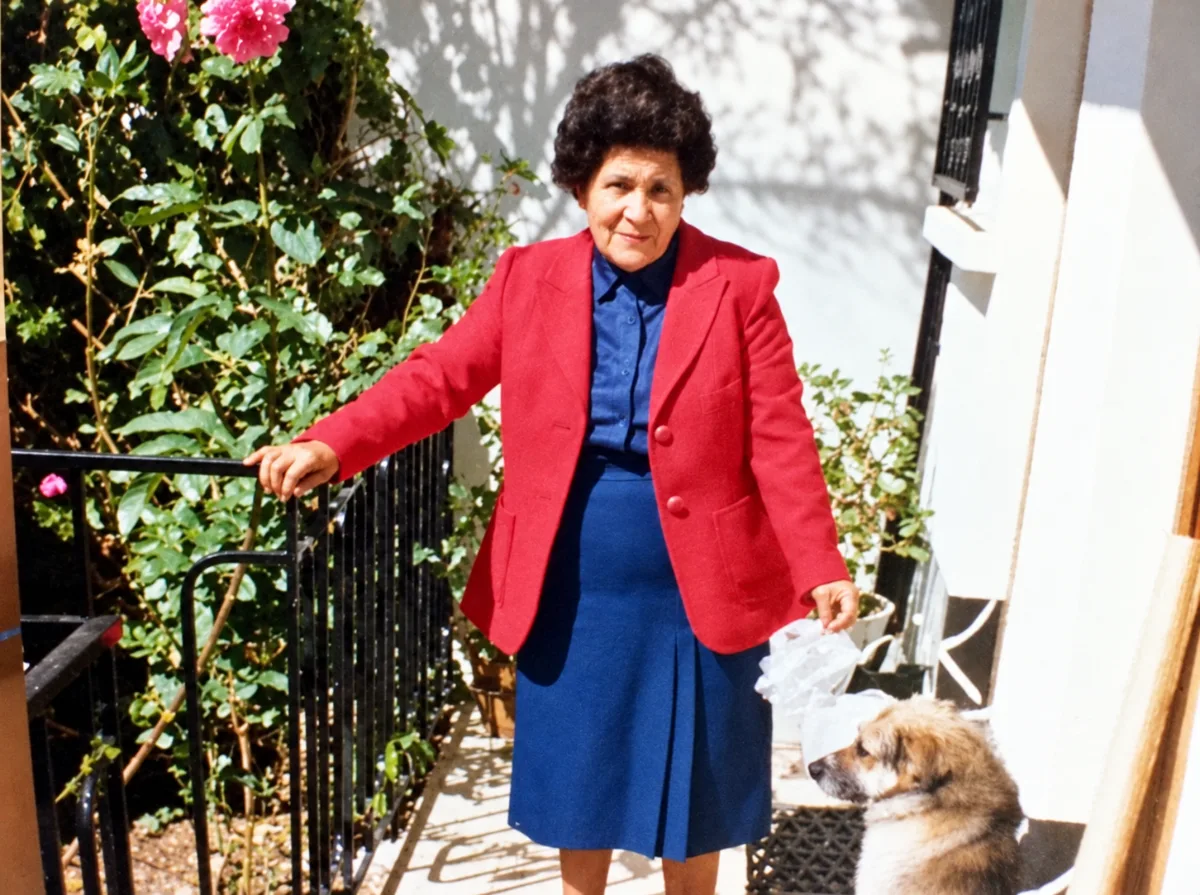 Yolanda con chaqueta roja junto a las flores de su casa